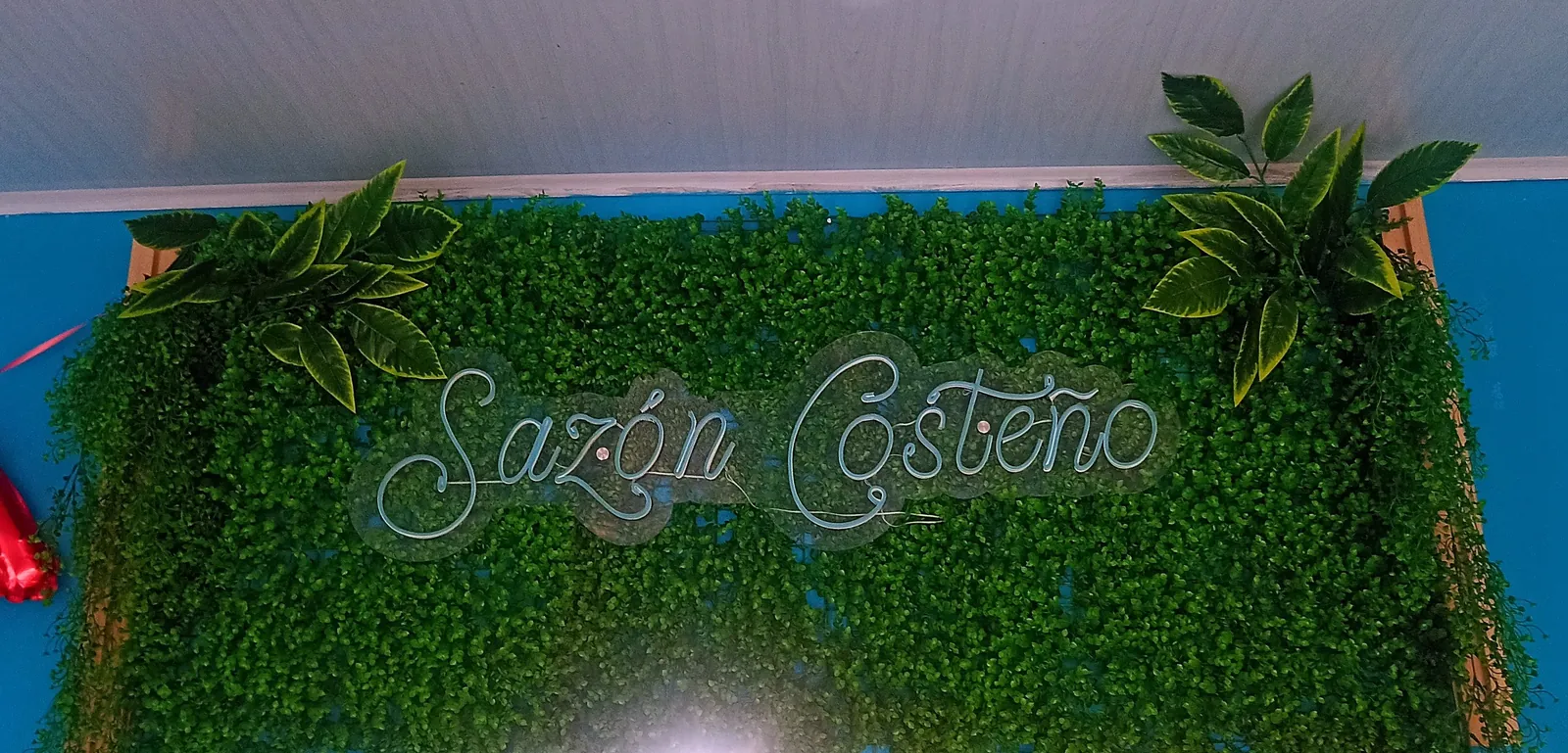 Letrero de neón «Sazón Costeño» sobre el jardín vertical